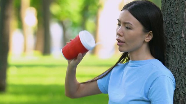 Girl drinking cocktail in plastic cup, throwing trash on grass, littering