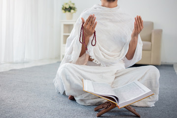 Muslim man praying while sitting in white traditional clothes
