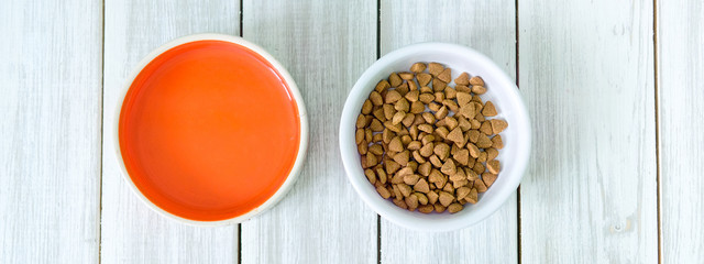 Dry cats food in a round bowl on white wooden floor overhead