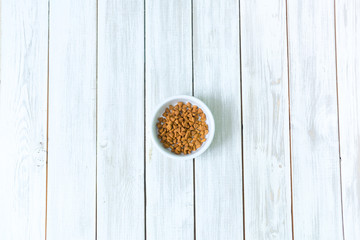 Dry cats food in a round bowl on white wooden floor overhead