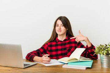 Young teenager going back to her routine doing homeworks person pointing by hand to a shirt copy space, proud and confident