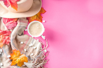 Autumn composition concept background. Cappuccino hot chocolate cup, with autumn bright leaves, pine cones, marshmallows, felt hat and blanket. Flatlay on pink trendy background, top view pattern