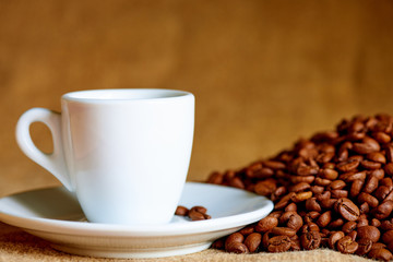 White cup and coffee beans on a blurred background.