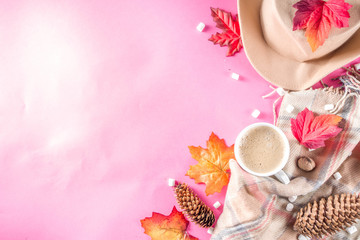 Obraz na płótnie Canvas Autumn composition concept background. Cappuccino hot chocolate cup, with autumn bright leaves, pine cones, marshmallows, felt hat and blanket. Flatlay on pink trendy background, top view pattern