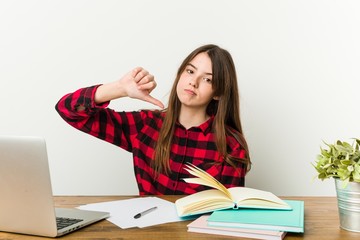 Young teenager going back to her routine doing homeworks showing a dislike gesture, thumbs down. Disagreement concept.
