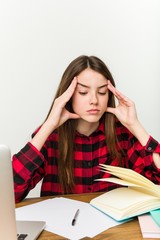 Young teenager going back to her routine doing homeworks touching temples and having headache.