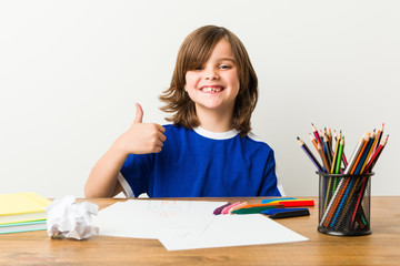 Little boy painting and doing homeworks on his desk smiling and raising thumb up