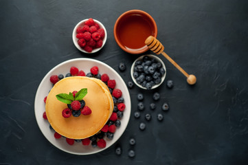 American pancakes with raspberries, fresh blueberries and honey. Healthy morning breakfast on concrete background