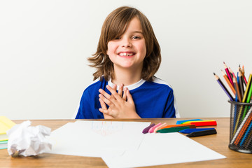 Little boy painting and doing homeworks on his desk has friendly expression, pressing palm to chest. Love concept.