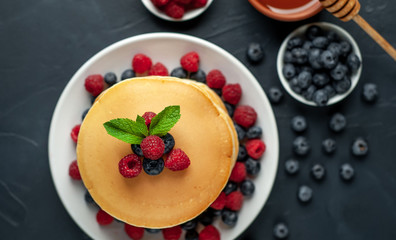 American pancakes with raspberries, fresh blueberries and honey. Healthy morning breakfast on concrete background
