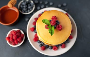 American pancakes with raspberries, fresh blueberries and honey. Healthy morning breakfast on concrete background