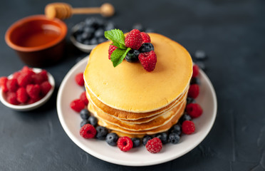 American pancakes with raspberries, fresh blueberries and honey. Healthy morning breakfast on concrete background