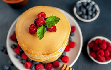 American pancakes with raspberries, fresh blueberries and honey. Healthy morning breakfast on concrete background