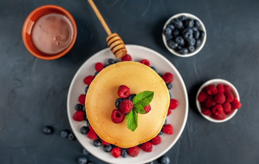 American pancakes with raspberries, fresh blueberries and honey. Healthy morning breakfast on concrete background