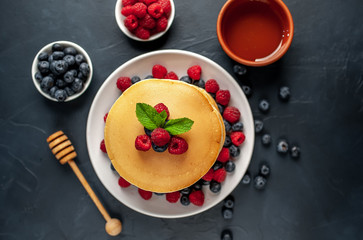 American pancakes with raspberries, fresh blueberries and honey. Healthy morning breakfast on concrete background