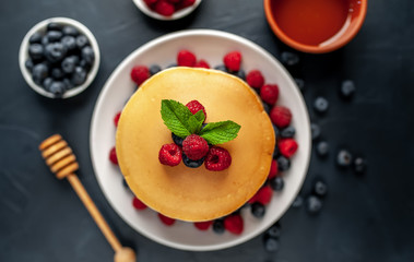 American pancakes with raspberries, fresh blueberries and honey. Healthy morning breakfast on concrete background