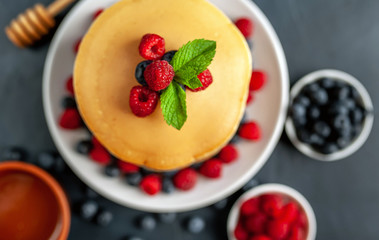 American pancakes with raspberries, fresh blueberries and honey. Healthy morning breakfast on concrete background