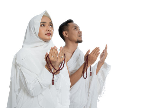 Muslim man and woman praying while standing in white traditional clothes ihram isolated over white background