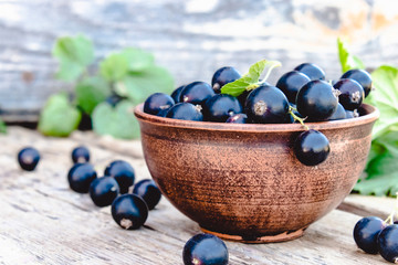 Fresh ripe currant berries in a bowl on wooden background near green leaves. Juicy fruits currants. Black currant