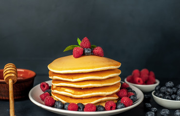 American pancakes with raspberries, fresh blueberries and honey. Healthy morning breakfast on concrete background