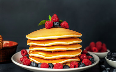 American pancakes with raspberries, fresh blueberries and honey. Healthy morning breakfast on concrete background