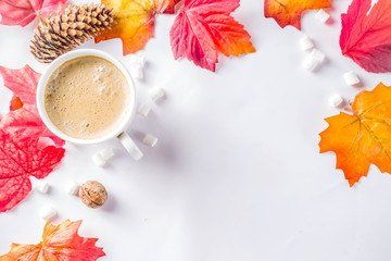 Autumn composition concept background. Cappuccino coffee or hot chocolate cup, with autumn bright leaves, pine cones, marshmallows. Flatlay on white background, simple top view pattern