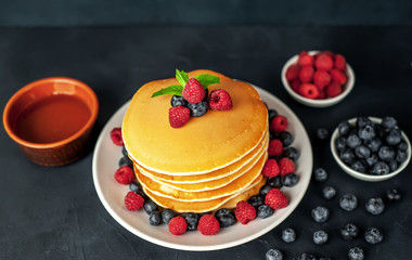 American pancakes with raspberries, fresh blueberries and honey. Healthy morning breakfast on concrete background
