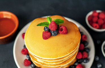 American pancakes with raspberries, fresh blueberries and honey. Healthy morning breakfast on concrete background