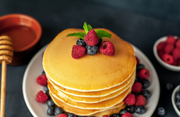 American pancakes with raspberries, fresh blueberries and honey. Healthy morning breakfast on concrete background