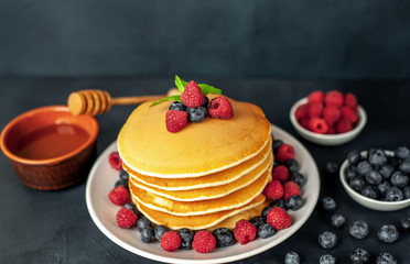 American pancakes with raspberries, fresh blueberries and honey. Healthy morning breakfast on concrete background