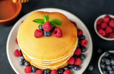 American pancakes with raspberries, fresh blueberries and honey. Healthy morning breakfast on concrete background