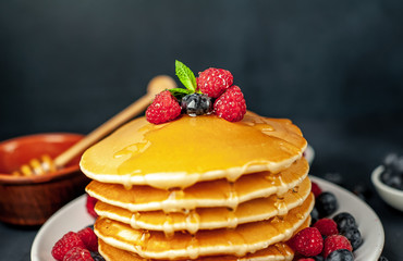 American pancakes with raspberries, fresh blueberries and honey. Healthy morning breakfast on concrete background