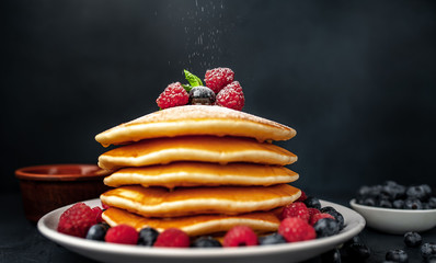 American pancakes with raspberries, fresh blueberries and honey. Healthy breakfast on concrete background, sprinkled with powdered sugar on pancakes