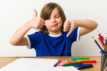 Little boy painting and doing homeworks on his desk showing thumbs up and thumbs down, difficult...