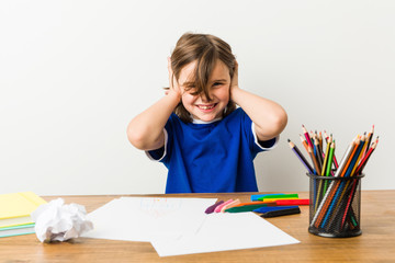 Little boy painting and doing homeworks on his desk covering ears with hands trying not to hear too...