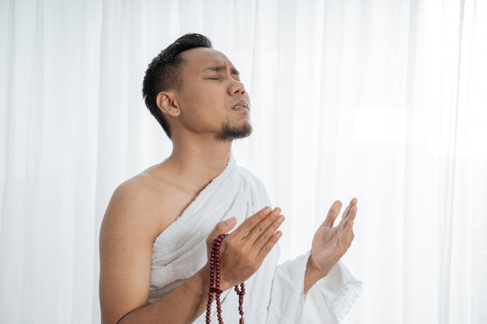 Muslim man praying while standing in white traditional clothes
