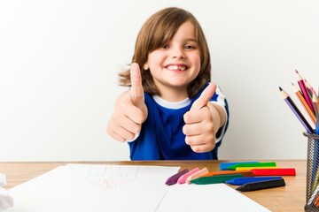 Little boy painting and doing homeworks on his desk with thumbs ups, cheers about something,...