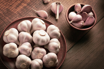 Top view heads of garlic in a ceramic dish and a cup on a wooden table in rustic style