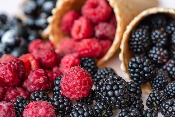 Raspberries, currants, blackberries closeup poured out of waffle cones, the focus is on raspberries