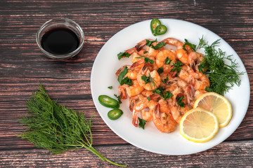 Fried shrimp in cream sauce with a plate on the table with lemon and dill, next to dill branches and soy sauce