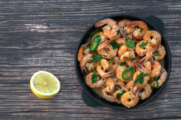 Fried shrimp in cream sauce in a cast iron pan on the table, next to half a lemon