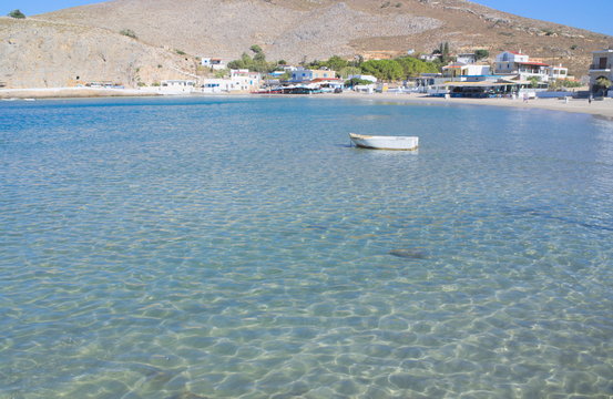 Greece, the island of Pserimos in the Dodecanese.  The harbor beach at Avalakia, before the day trip boats arrive.  A bright and sunny September day. A lone little boat at anchor.