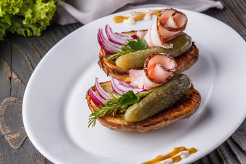 Halves baked potato with pickled cucumber, dill, salo and onion on wooden table