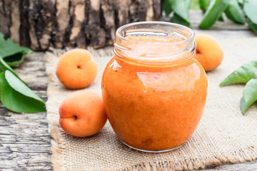 Homemade organic jam in a glass jar and ripe apricots on a wooden table.