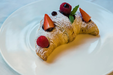Croissant su piatto bianco con decorazioni di frutta, cioccolato e zucchero a velo