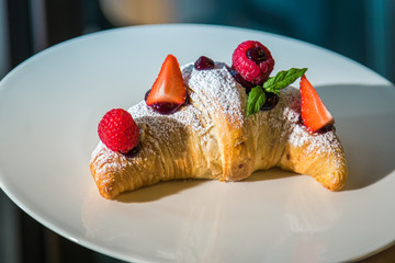 Croissant su piatto bianco con decorazioni di frutta, cioccolato e zucchero a velo