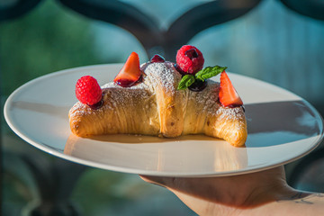 Croissant su piatto bianco con decorazioni di frutta, cioccolato e zucchero a velo