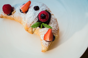 Croissant su piatto bianco con decorazioni di frutta, cioccolato e zucchero a velo