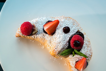 Croissant su piatto bianco con decorazioni di frutta, cioccolato e zucchero a velo