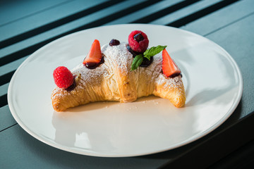 Croissant su piatto bianco con decorazioni di frutta, cioccolato e zucchero a velo